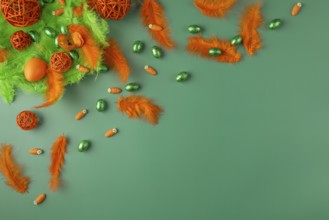 Decorative arrangement with feathers and chocolate eggs in green and orange on a green surface