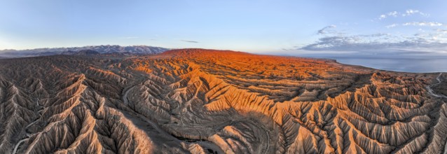 Panorama, landscape of eroded hills at Lake Issyk Kul, badlands at sunrise, mountain peaks of the