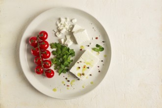 Feta cheese, for salads, with cherry, green butter, greens, on a white plate, appetizer, top view,