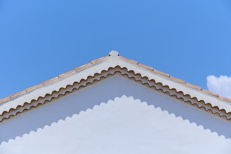 Top of a white painted house with a red tiled roof against a clear blue sky, summer,