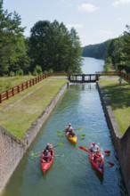 Three kayaks travelling through a narrow forest channel under a clear sky in nature, Sluza Paniewo,