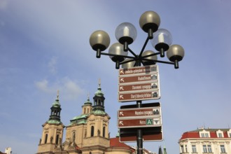 A street lamp on the Old Town Square with signs of the sights in the city and the towers of the