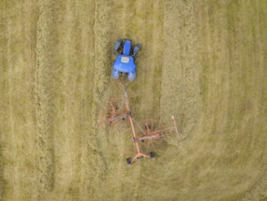 An aerial view shows a tractor with a hay tedder ploughing patterns into a hay field, Dachtel.