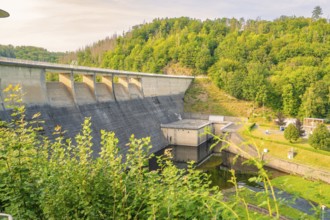 Large dam in a wooded landscape in sunny weather with green foliage and blue sky,