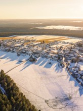 Aerial view of a snow-covered village next to a dense forest in the soft light of late afternoon,