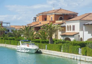 Leisure boat at quay in canal and with palm trees and holiday homes in Lido di Policoro resort,