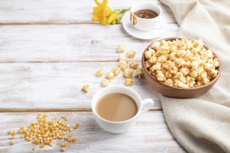 Popcorn with caramel in wooden bowl and a cup of coffee on a white wooden background and linen