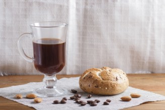 Glass cup of coffee with bun on a wooden background and linen textile. close up, copy space