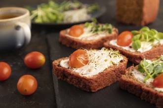 Red beet bread sandwiches with cream cheese, tomatoes and microgreen on black concrete background.