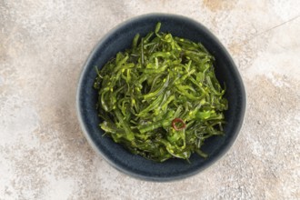 Chuka seaweed salad in blue ceramic bowl on brown concrete background. Top view, flat lay