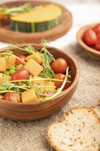 Vegetarian vegetable salad of tomatoes, pumpkin, microgreen pea sprouts on white wooden background