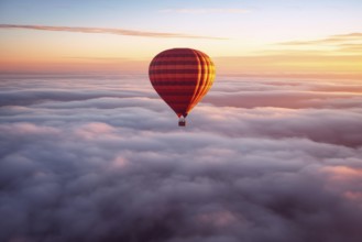 Colorful hot air balloon floats over a sea of clouds at sunset at sunset with orange and blue skies