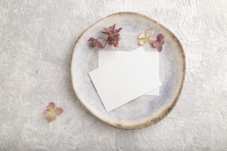 White paper invitation card, mockup with dried hydrangea flowers on ceramic plate and gray concrete