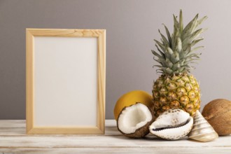 Wooden frame with melon, coconut, pineapple, seashells on gray pastel background. Side view, copy