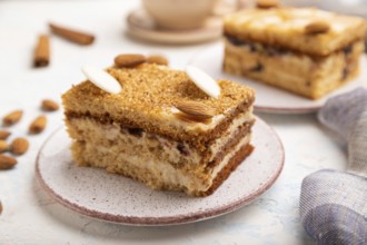 Honey cake with milk cream, caramel, almonds and a cup of coffee on a white concrete background and