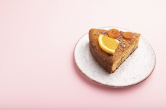 A piece of orange cake on a pastel pink background. Side view, copy space, close up