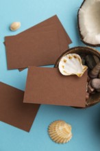 Brown paper business card with coconut and seashells on blue pastel background. Top view, flat lay,