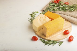 Various types of cheese with rosemary and tomatoes on wooden board on a white wooden background and