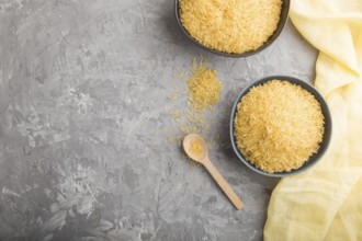 Blue ceramic bowl with raw golden rice and wooden spoon on a gray concrete background and yellow