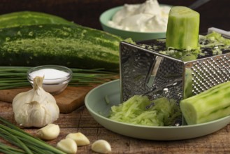 Fresh ingredients such as grated cucumber, garlic, chives and sour cream on a wooden table