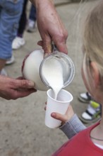 Farmer pouring fresh milk in little girl's plastic cup at farm