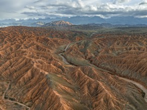 River bed runs through a landscape of eroded hills, badlands at sunset, mountain peaks of the Tian