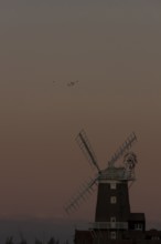 Windmill at sunset with a red sky and a skein or flock of Pink-footed geese (Anser brachyrhynchus)