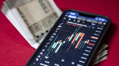 Stock market graph or chart display on a mobile phone against Indian 500 rupee paper currency note