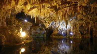 Illuminated cave landscape with water reflection and stalactites from above, stalactite cave, Diros