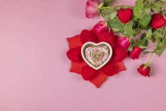 Bouquet of roses next to a heart-shaped bowl with a muffin surrounded by red hearts on a pink