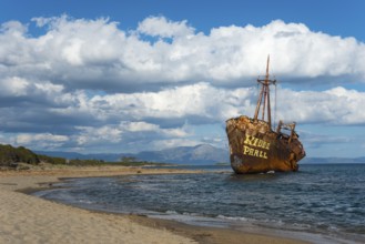 A rust-coloured shipwreck protrudes from a calm stretch of sea under a cloudy sky, Dimitrios