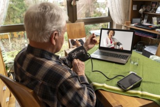 Symbolic image of telemedicine, elderly patient speaks to a doctor in a video conference from home,