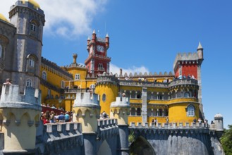 Colourful castle with yellow, red and grey towers, blue sky and visitors, Palácio Nacional da Pena,