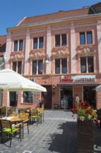 Street view of a pink façade with elaborate stucco details and a café in the foreground, town house