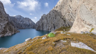 Green tent by a blue mountain lake between steep rocky mountain peaks, Kol Suu Lake, Sary Beles