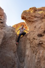 Young woman climbing between red sandstone rocks, erosion landscape of red and yellow sandstone,