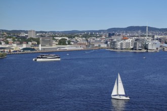 Urban coastal view with a sailing boat, modern harbour and surrounding buildings, electric ferry,