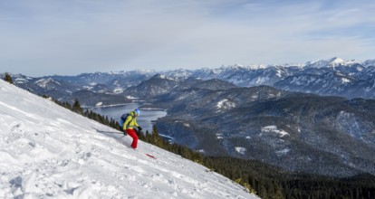 Skiers skiing down the Simetsberg, view of Walchensee and mountain panorama, Estergebirge, Bavarian