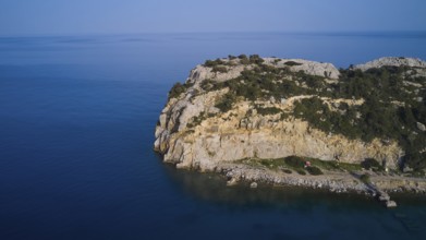 A drone shot shows a remote coastal strip with steep cliffs at the edge of the clear blue sea,