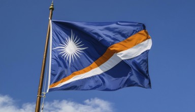 The flag of the Marshall Islands, Pacific Islands, flutters in the wind, isolated against a blue