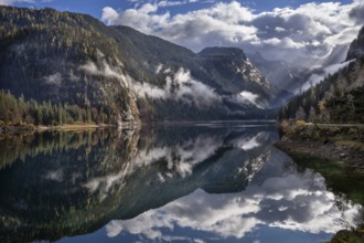 The Vordere Gosausee in autumn. In the background, the Dachstein mountain range in clouds. Partly