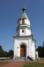 Detailed view of a white church with a green tower, surrounded by landscaped paths under a blue