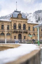 An imposing historic building in winter, surrounded by snow and wooded hills, König-Karls-Bad, Bad