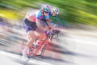 Two female cyclists in sportswear and helmets riding at high speed on a road, racing, the blur of