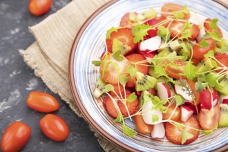 Vegetarian fruits and vegetables salad of strawberry, kiwi, tomatoes, microgreen sprouts on black