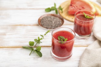 Watermelon juice with chia seeds and mint in glass on a white wooden background with linen textile.