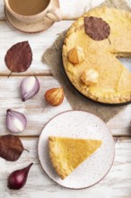 Autumn onion pie decorated with leaves and cup of coffee on white wooden background and linen