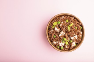 Quinoa porridge with green pea and chicken in wooden bowl on a pastel pink background. Top view,