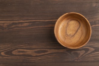 Empty brown wooden bowl on brown wooden background. Top view, copy space, flat lay