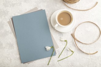 Blue paper sheet mockup with spring snowdrop galanthus flowers and cup of coffee on gray concrete